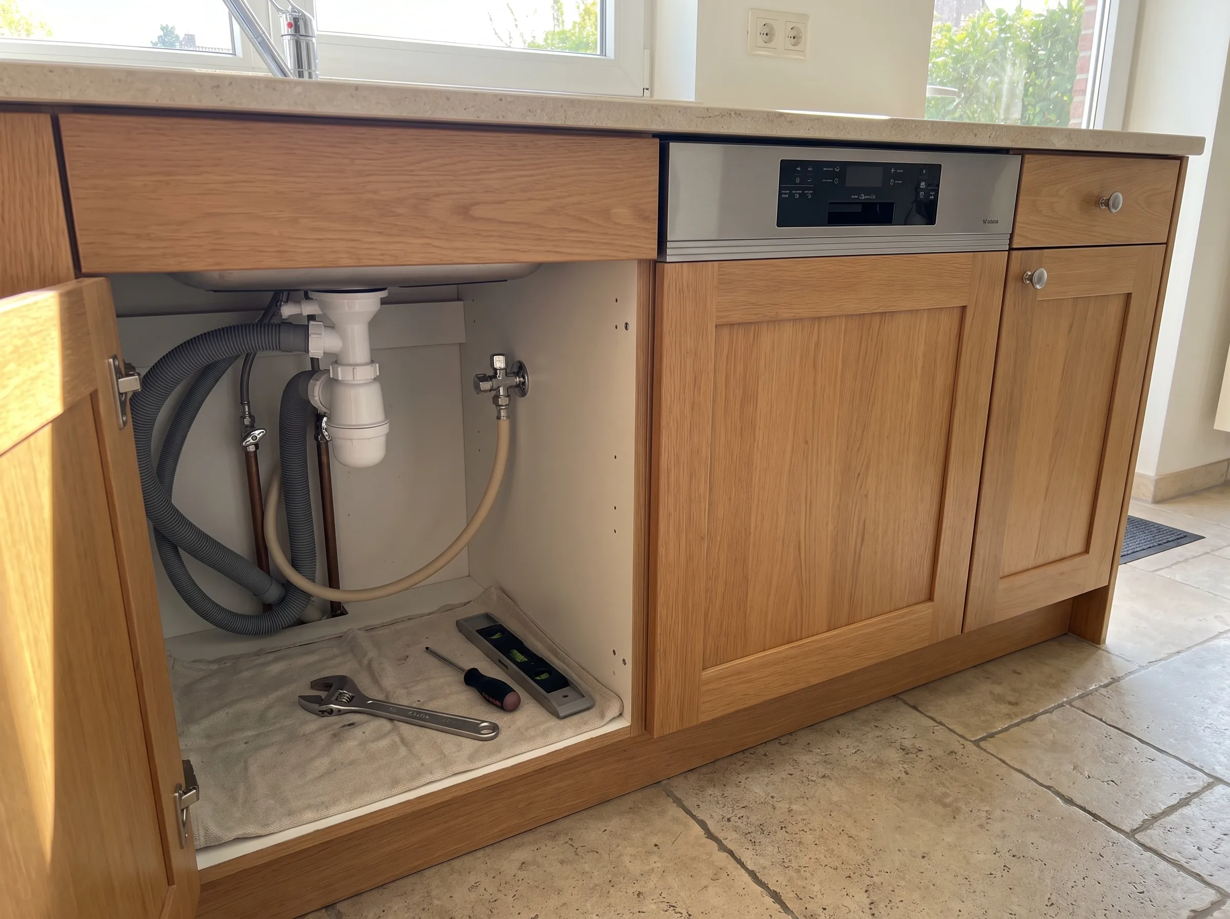 Onderkast van een keuken met sanitair leidingen en gereedschap zichtbaar