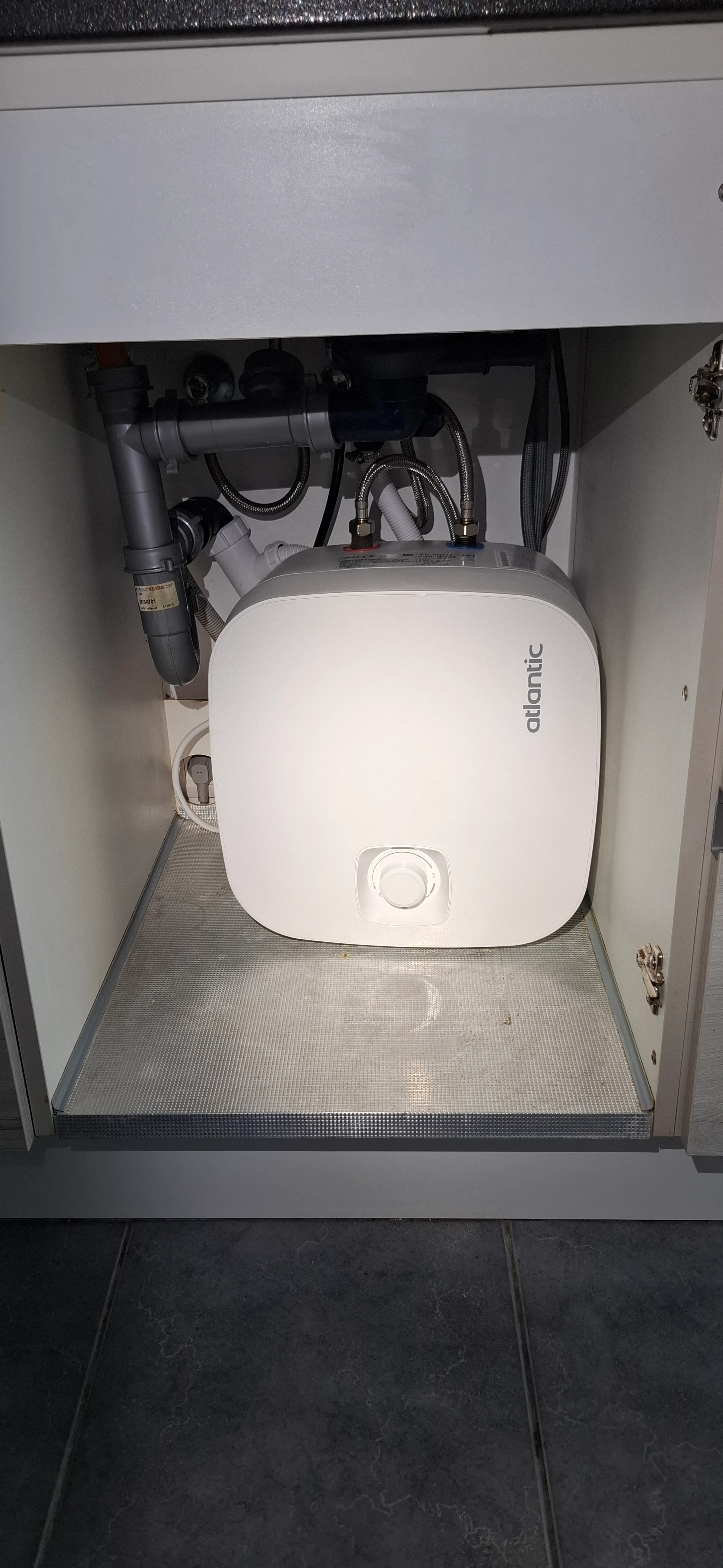 Warmwaterboiler geplaatst onder de aanrecht, met leidingen zichtbaar