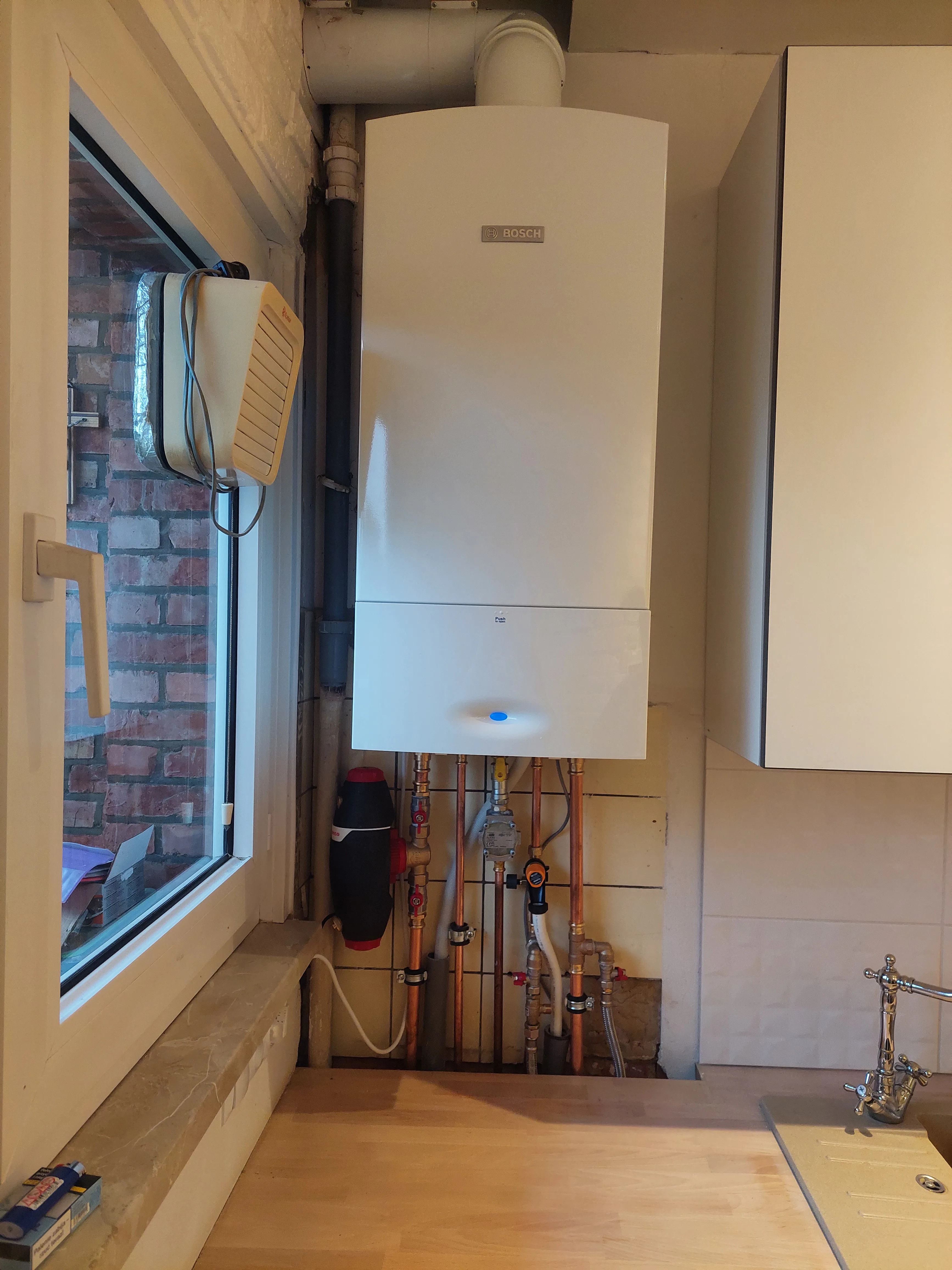 Installatie van een nieuwe gasketel in een keuken met leidingen zichtbaar