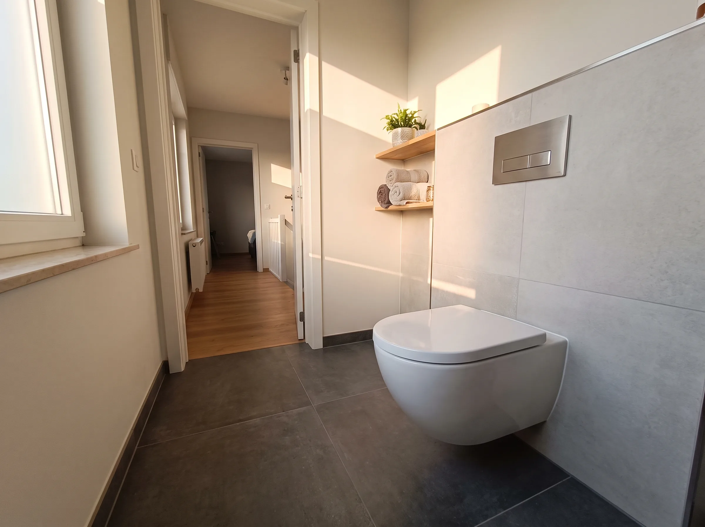 Moderne badkamer met hangend toilet, grote tegels en natuurlijk lichtinval
