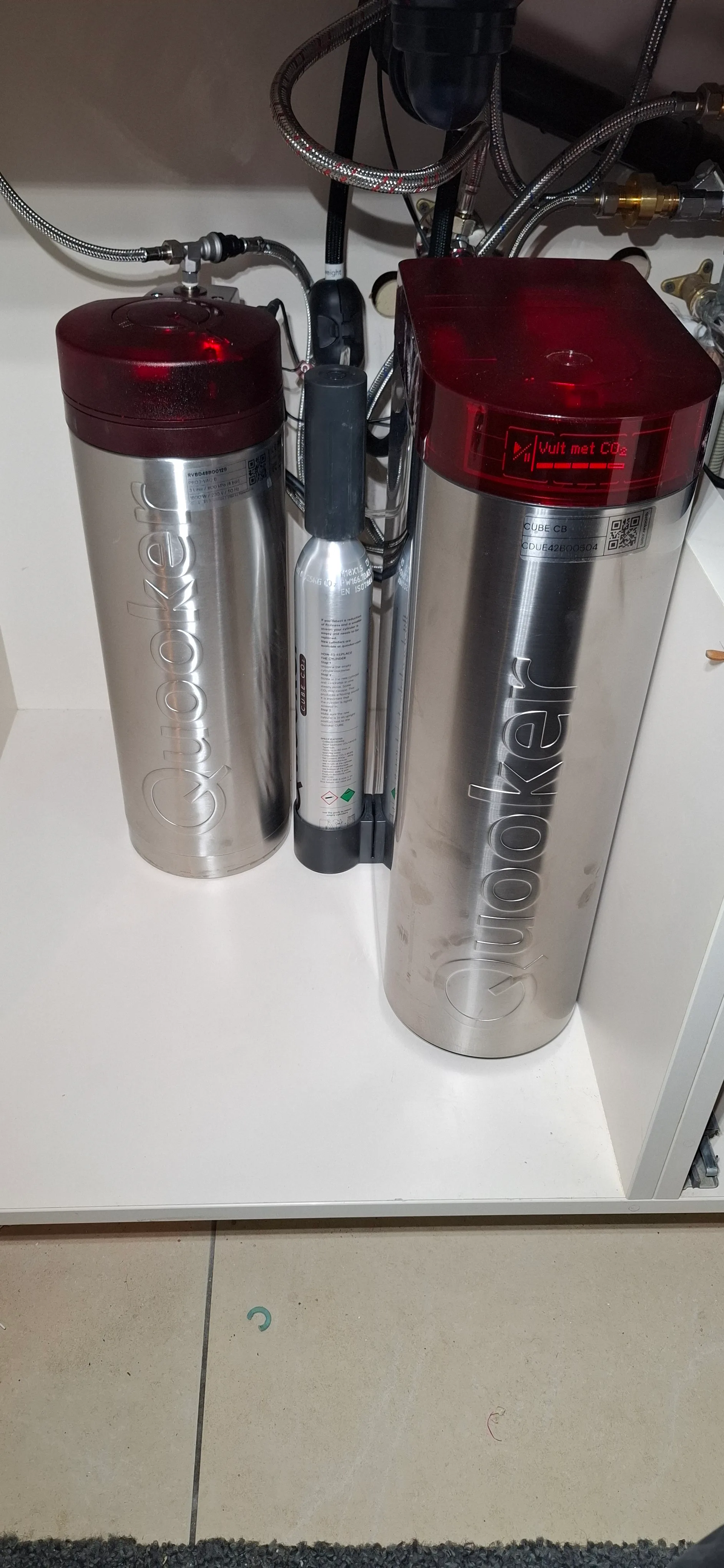 Twee Quooker-onderdelen op een witte kast voor warmwaterinstallatie
