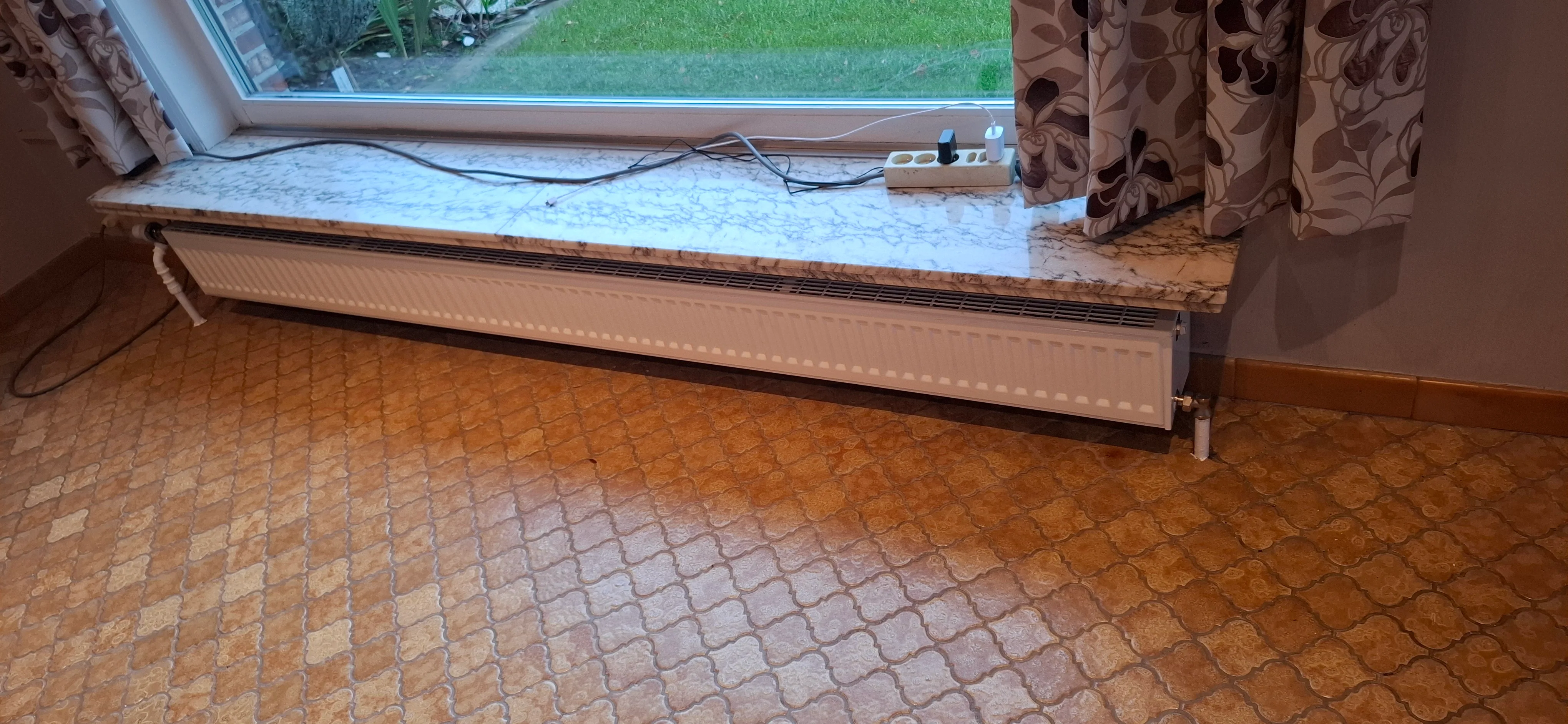 Radiator geplaatst onder een groot raam met zicht op de tuin