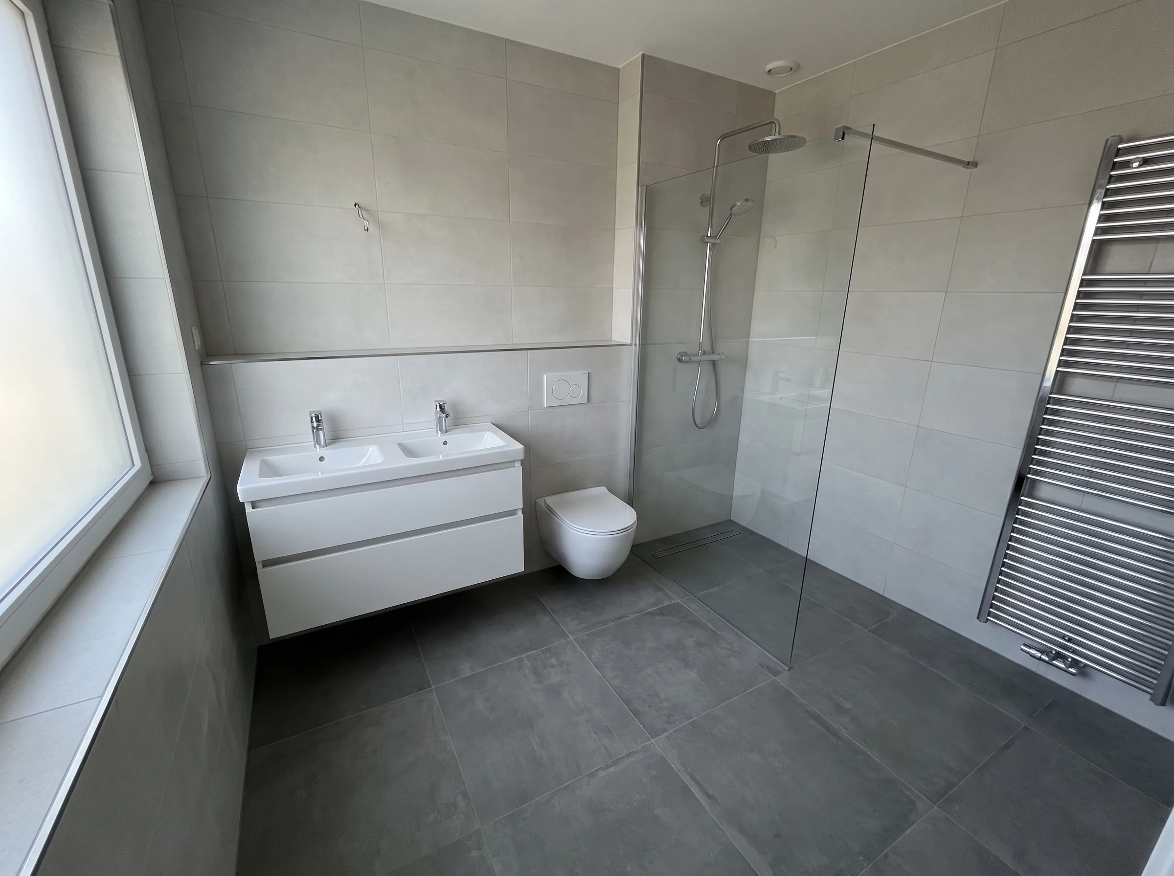 Moderne badkamer met inloopdouche, wastafels en verwarmingsradiator