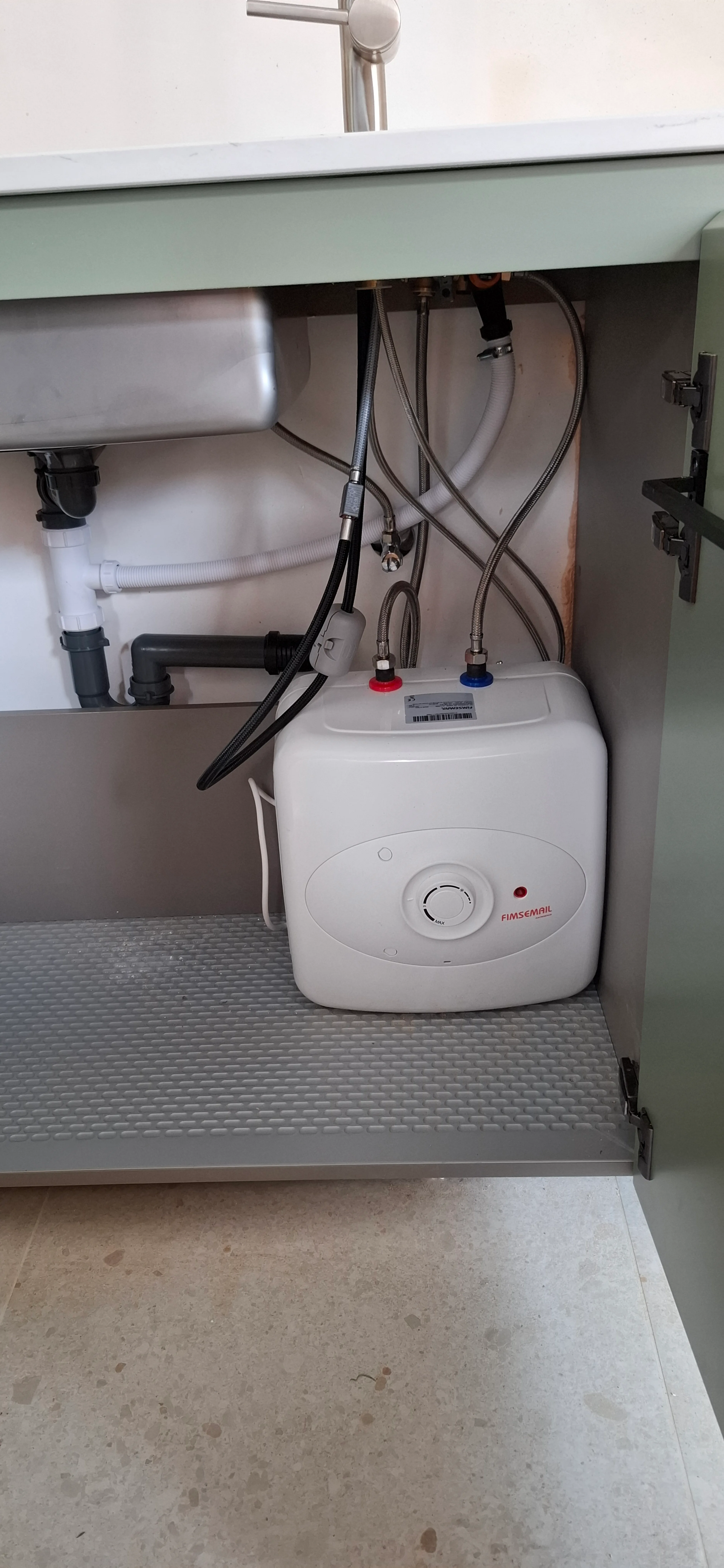 Warmwaterboiler geplaatst onder een keukenkastje met leidingen zichtbaar