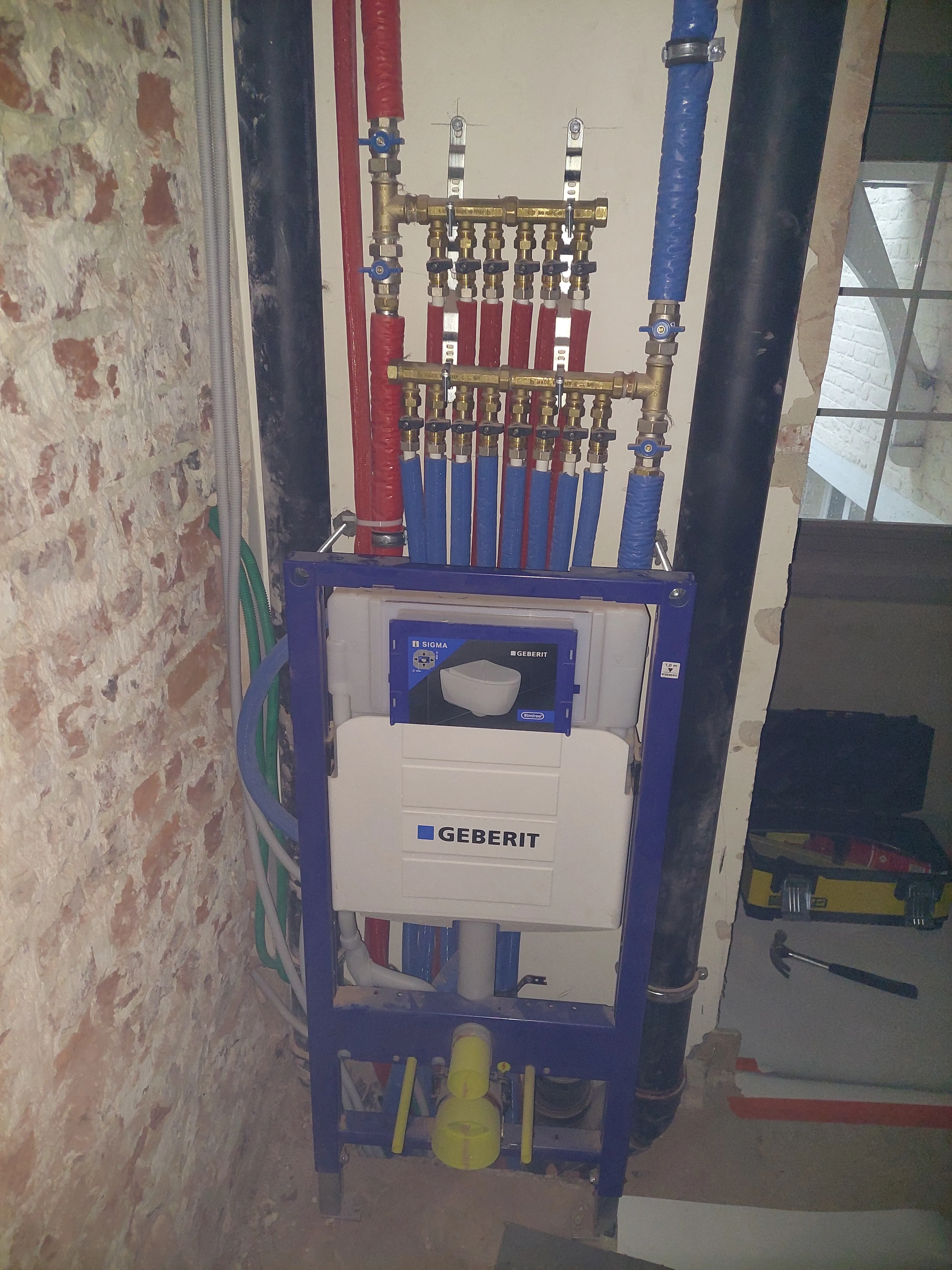 Installatie van een Geberit sanitair systeem met kleurrijke leidingen en aansluitingen